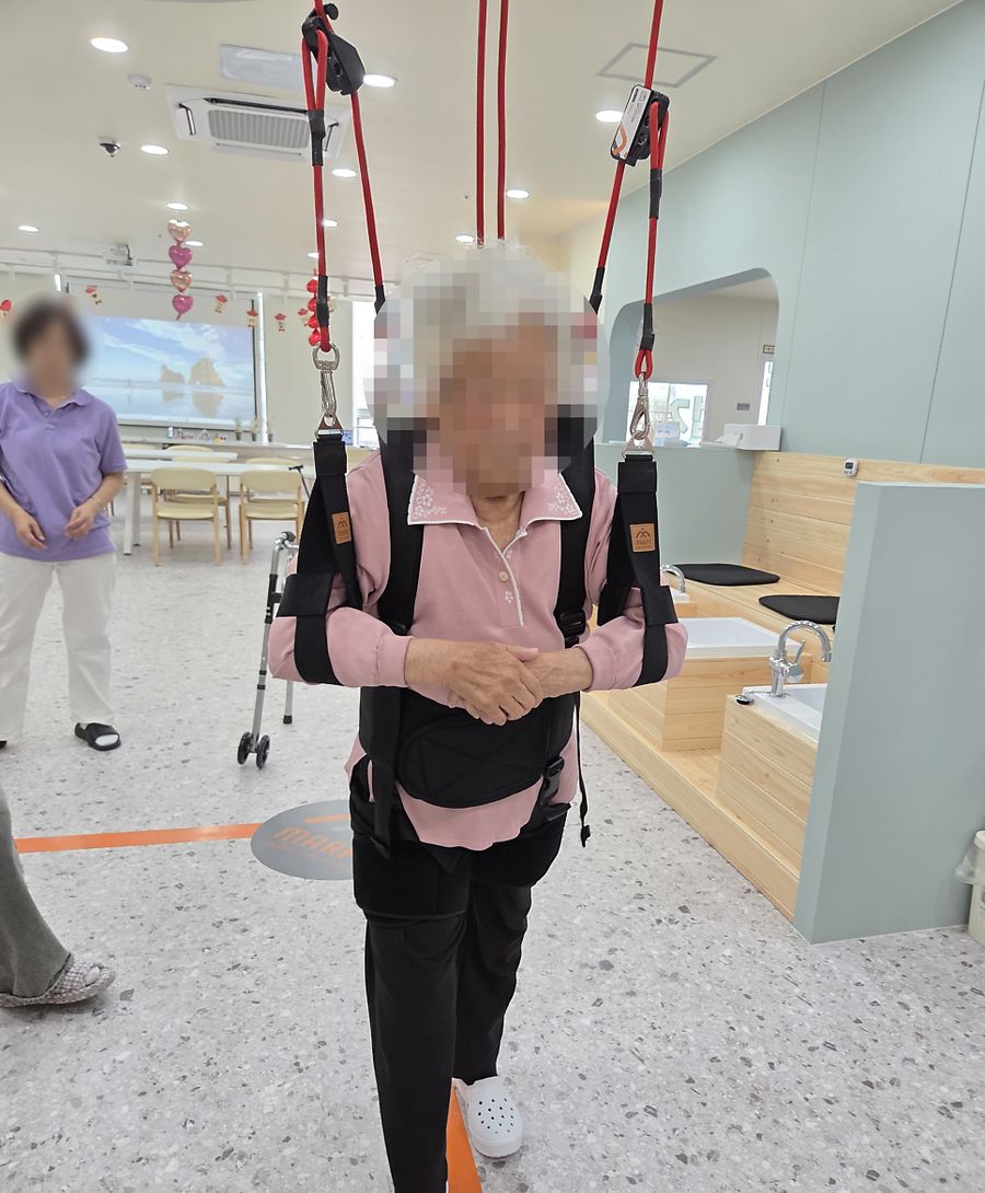 천장 레일의 슬링 조끼를 입고 걷기 연습을 하는 어르신